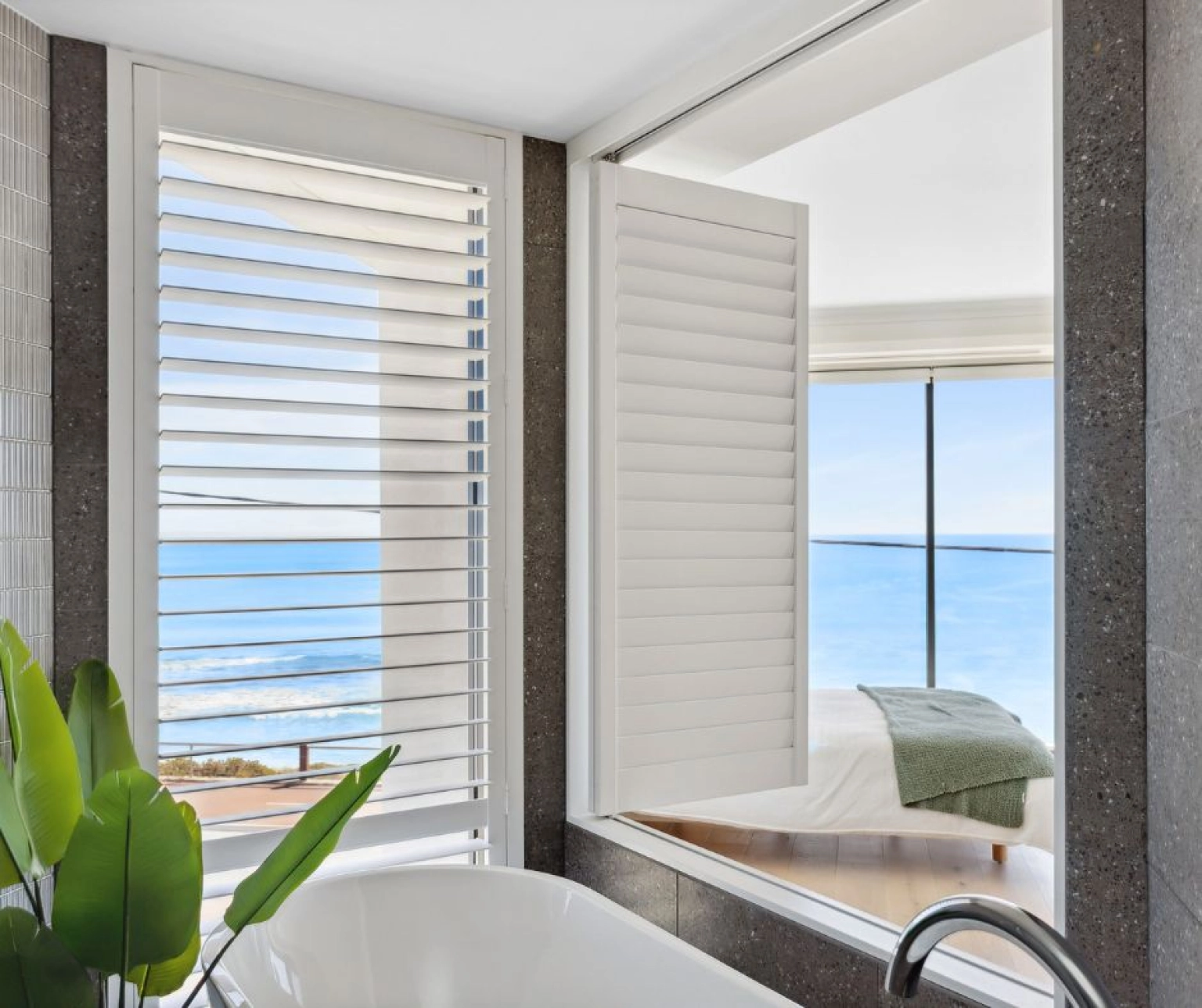Close up of bathroom window with shutters and ocean visible in background